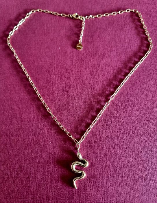 Colar dourado, em aço, com pingente em formato cobra. Tem extensor