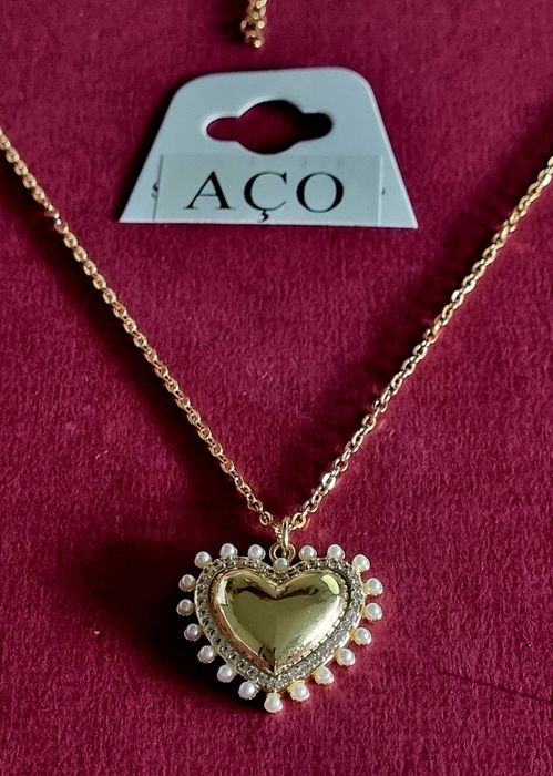 Colar dourado, em aço, com pingente formato coração rodeado de zirconias e pérolas