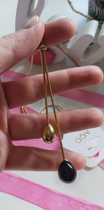 Colar dourado, em aço, com pedra preta. Estilo gravata