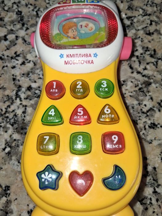 Telefone de criança. Tem musica nas teclas. Acende as luzes e muda a imagem no visor simulando uma televisão.