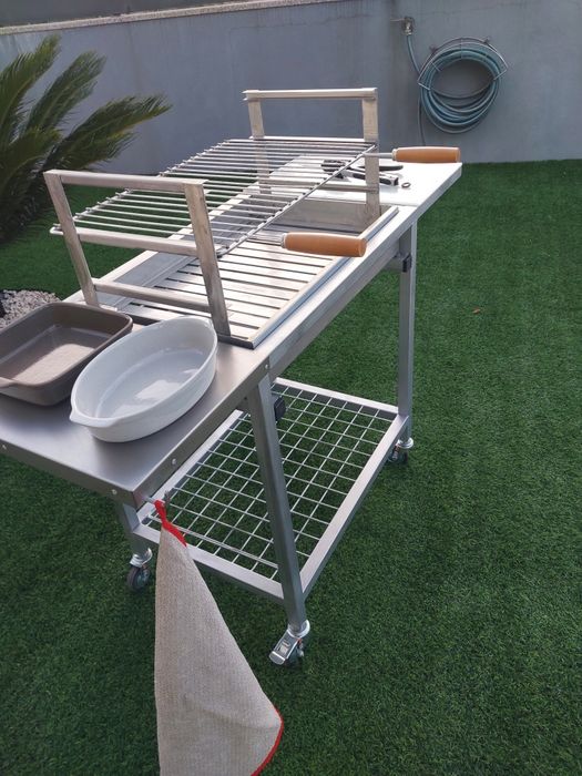Churrasqueira com rodas, tem queimador  e grelha em inox  duas mesas de apoio uma em inox outra em nylon  e plataforma para lenha..