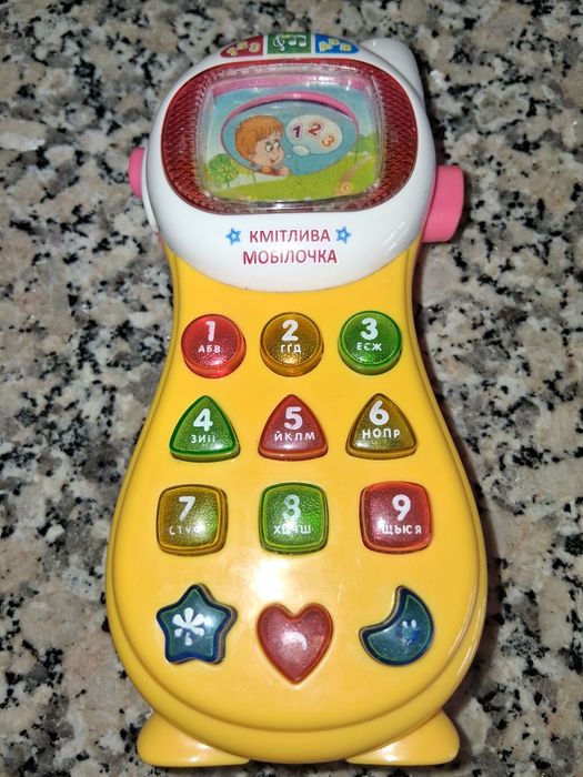 Telefone de criança. Tem musica nas teclas. Acende as luzes e muda a imagem no visor simulando uma televisão.