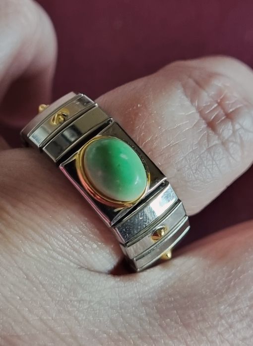 Anel prateado, em aço, com apontamentos dourados e pedrinha verde.