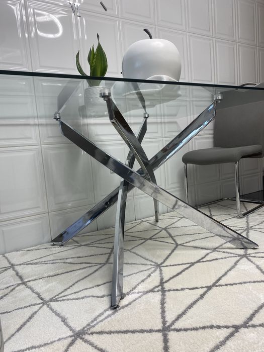 4 cadeiras mais mesa de jantar moderna  com um tampo em vidro transparente e uma elegante estrutura de pernas cruzadas em aço cromado brilhante.