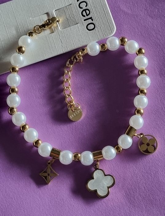 Pulseira dourada, em aço, com pérolas e um trevo branco. Tem extensor