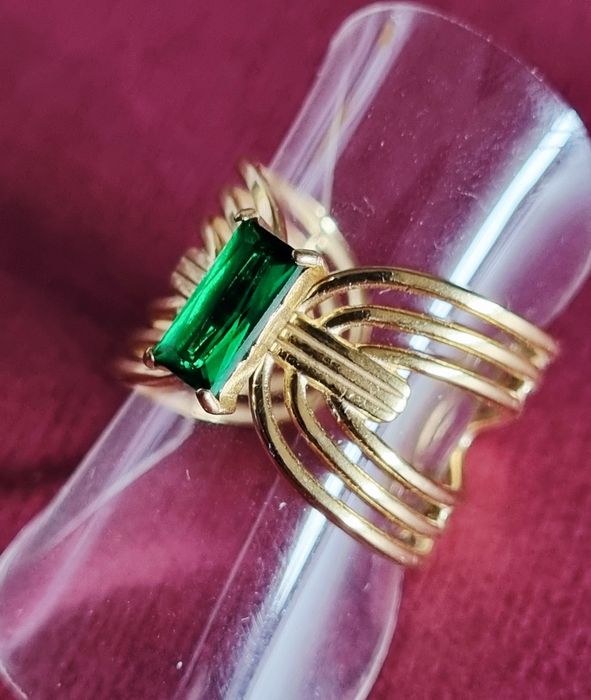 Anel dourado, em aço, com pedrinha retangular verde no centro. Ajustável