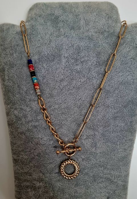 Colar dourado, em aço, assimétrico e com pedrinhas naturais coloridas.