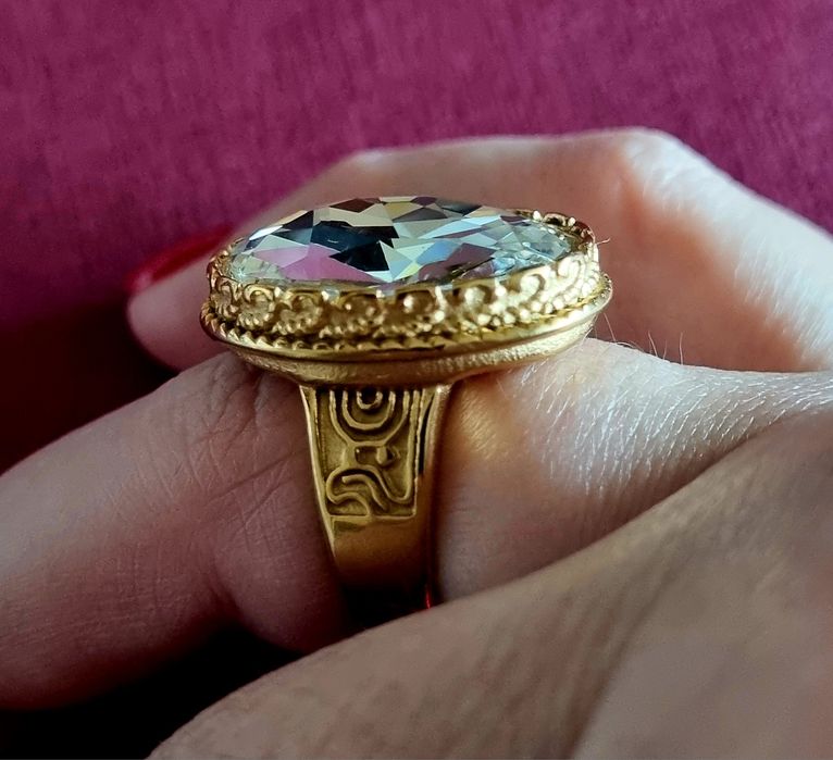 Anel dourado, em aço, com grande pedra de vidro transparente oval. T17