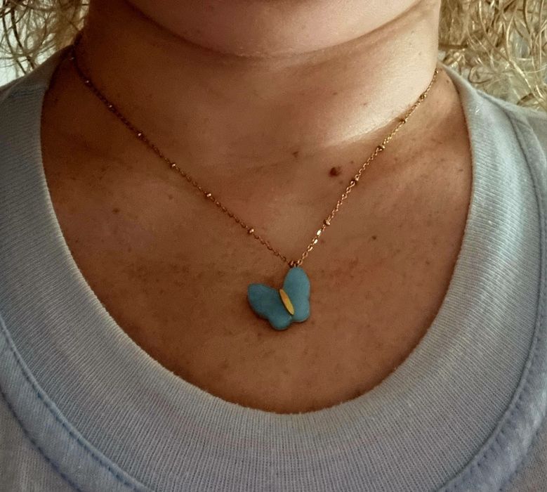Colar dourado, em aço, malha com bolinhas e pingente borboleta azul.