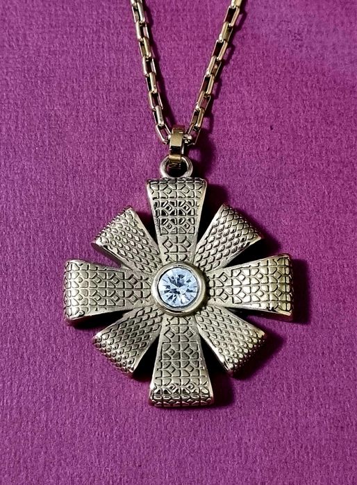 Colar dourado, em aço, com flor trabalhada e um ponto de luz central.