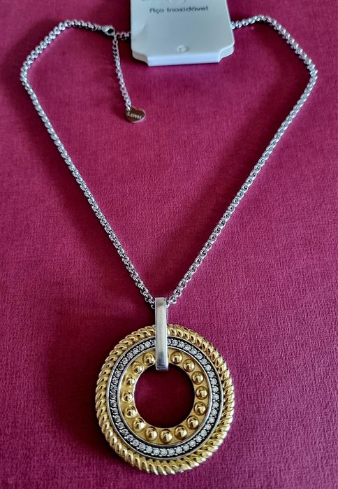 Colar prateado, em aço, com pingente bicolor. Tem extensor