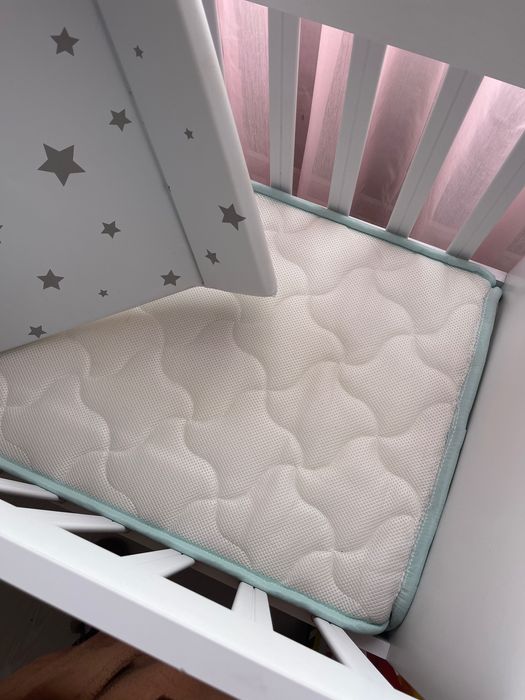 Berço de bebê com balanço, com um colchão e um trocador de fraldas.