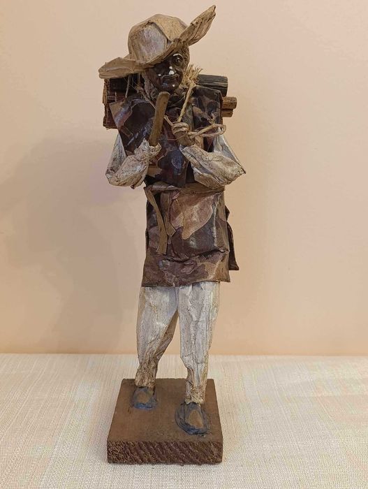 Handcrafted figure of a man carrying a bundle of firewood on his back, papier-mâché