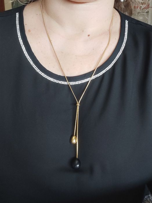 Colar dourado, em aço, com pedra preta. Estilo gravata