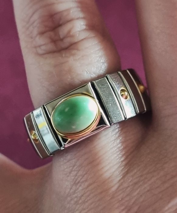 Anel prateado, em aço, com apontamentos dourados e pedrinha verde.