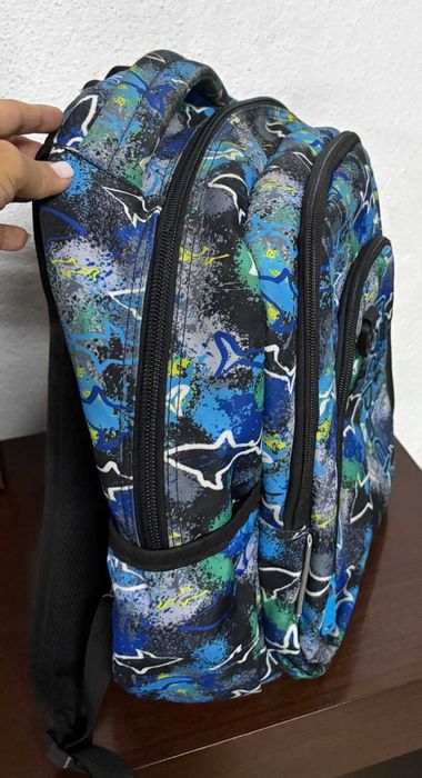 Mochila escolar CoolPack em tons azul, verde e preto, com padrão de tubarões.