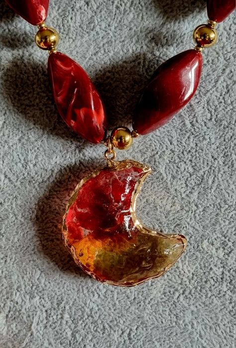 Colar dourado, em aço, com peças bordeaux em acrílico e uma meia lua.
