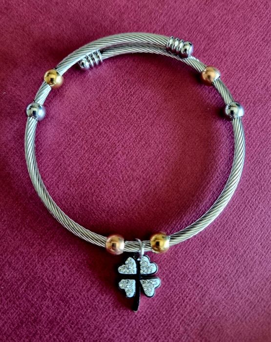 Pulseira prateada, em aço, com bolinhas douradas e um trevo da sorte.