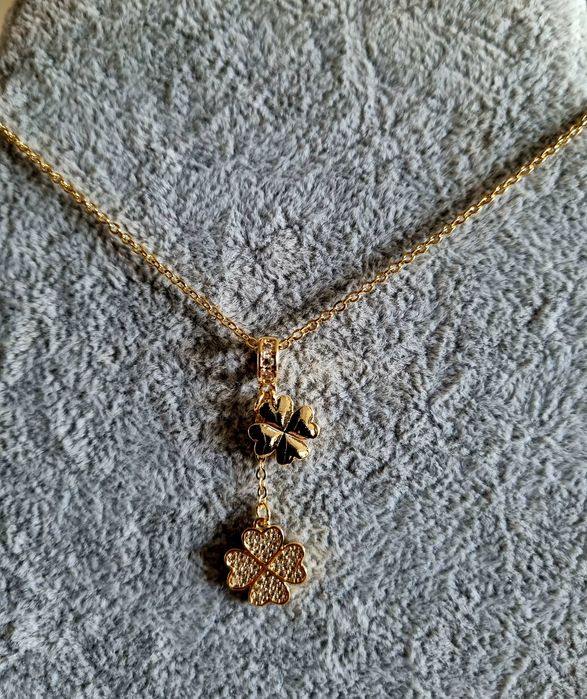 Colar dourado, em aço, com 2 trevos pendentes. Formato gravata.