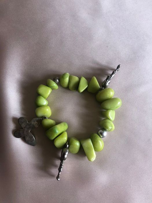 Pulseira com pedras verdes e elementos metálicos como o trevo e outros