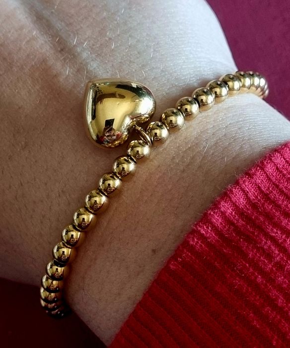 Pulseira dourada, em aço, toda às bolinhas e com 1 coração. Tem extens