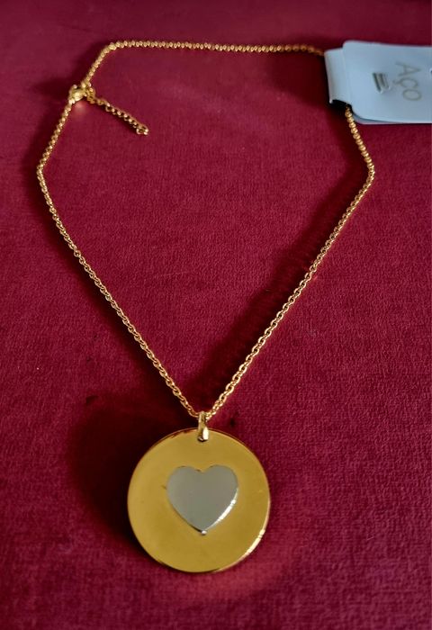 Colar dourado, em aço, com pingente redondo dourado e um coração prateado no centro