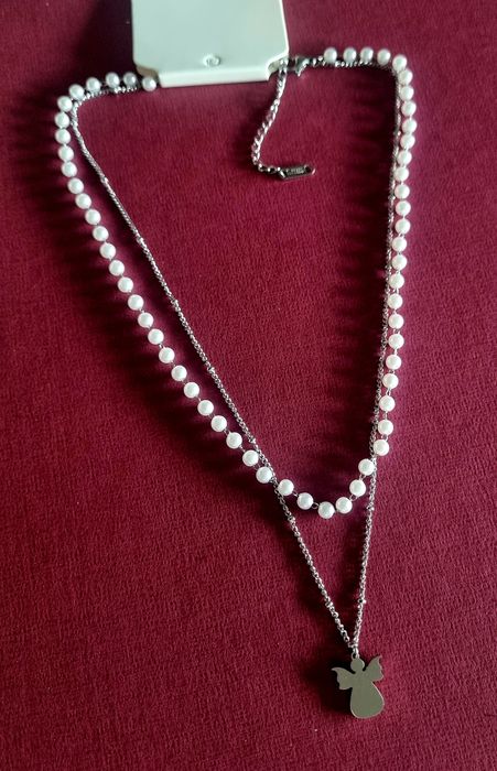 Colar duplo, em aço, 1 de pérolas e 1 com anjinho. Tem extensor