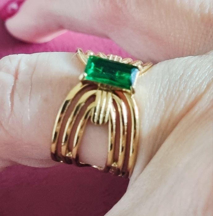 Anel dourado, em aço, com pedrinha retangular verde no centro. Ajustável
