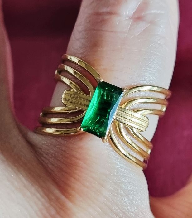 Anel dourado, em aço, com pedrinha retangular verde no centro. Ajustável