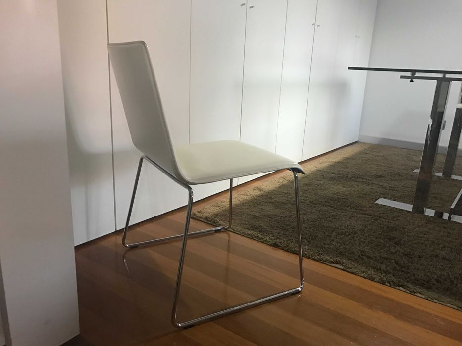 quatro cadeiras de pele branca e base em inox