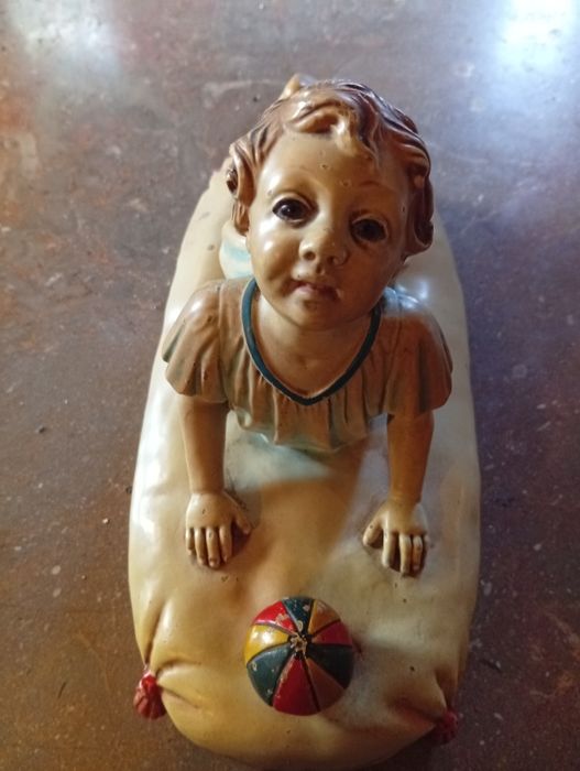 Figura cerâmica de bebé sobre uma almofada com uma bola