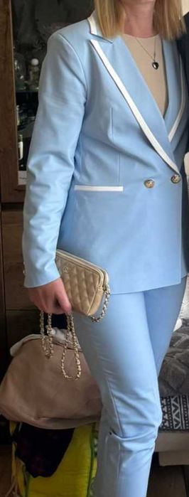 Elegancki damski garnitur, niebieski żakiet i spodnie z białymi lamówkami.