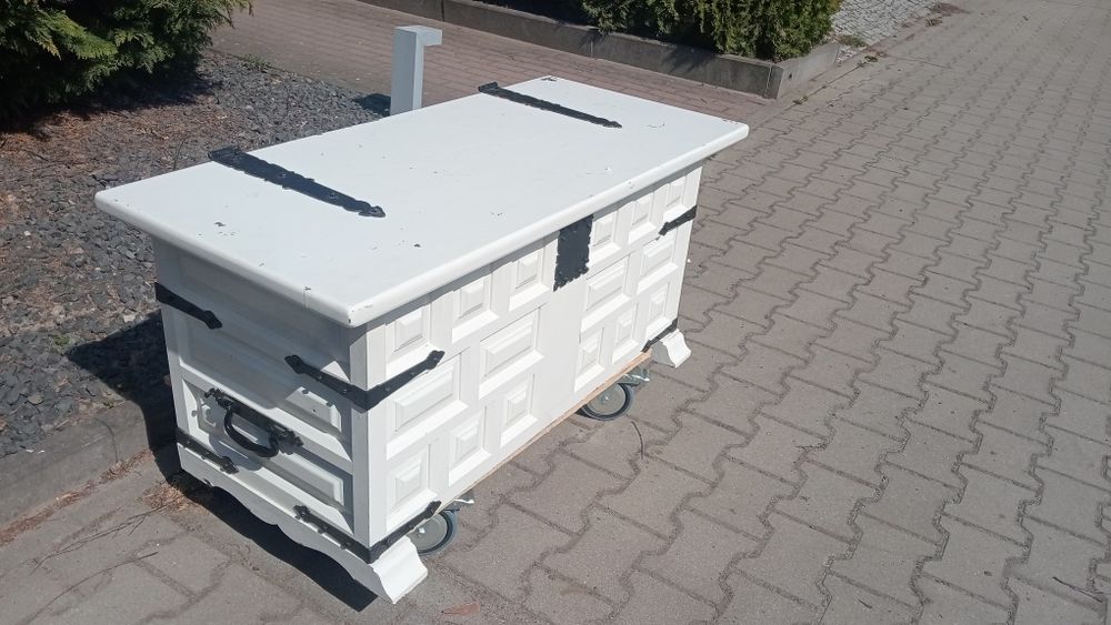 Biała duża skrzynia, kufer z czarnymi okuciami.