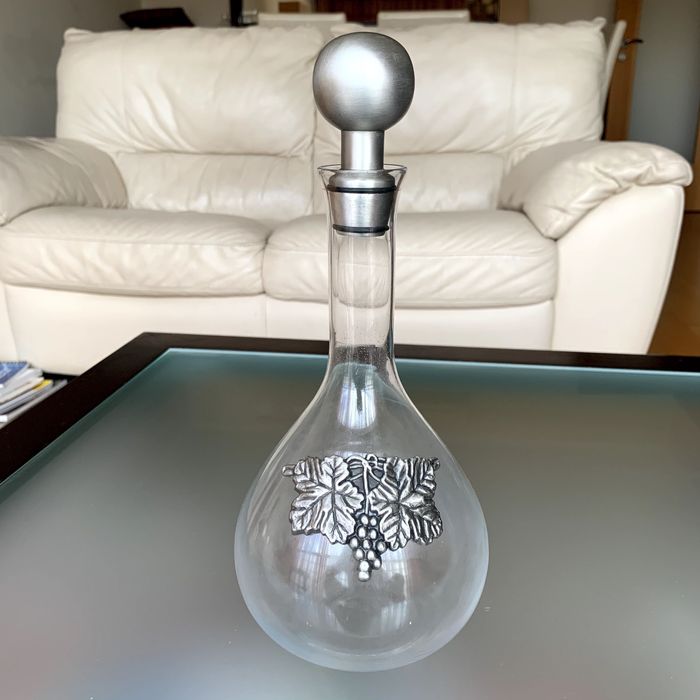 Licoreira de vidro com pormenor decorativo e rolha metálicos.