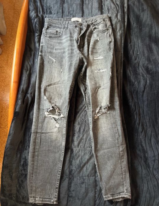 Calças de ganga cinza escura, com detalhes de rasgos