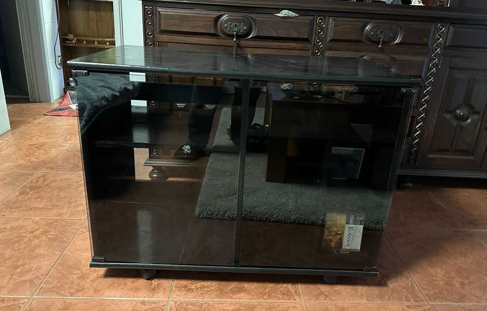 Móvel TV preto com portas de vidro e rodas.