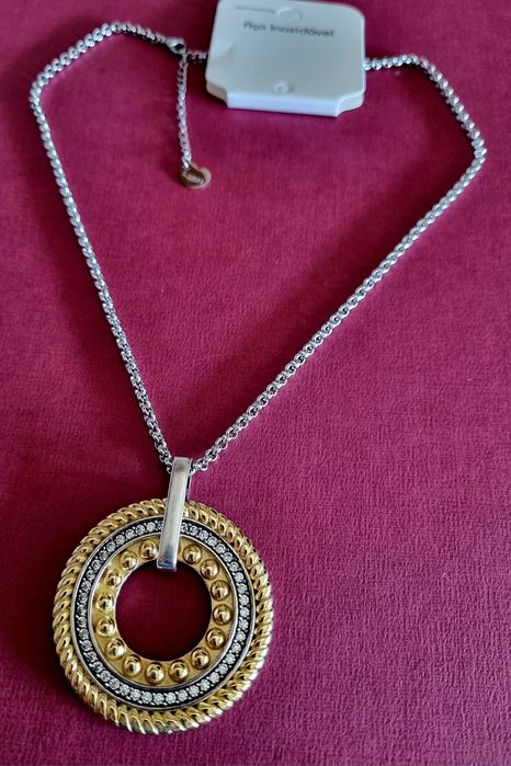 Colar prateado, em aço, com pingente bicolor. Tem extensor