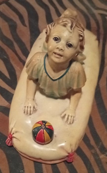 Figura cerâmica de bebé sobre uma almofada com uma bola