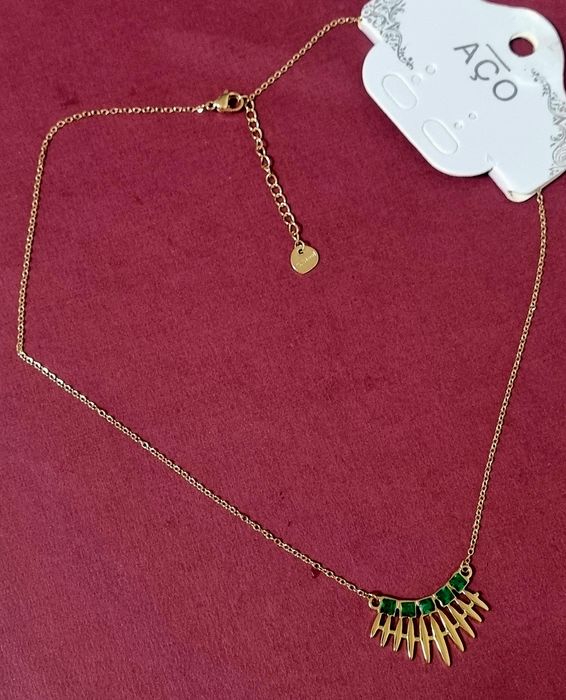 Colar dourado, em aço, com 5 pedrinhas quadradas verdes. Tem extensor.
