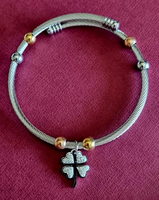 Pulseira prateada, em aço, com bolinhas douradas e um trevo da sorte.