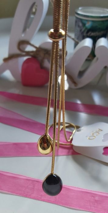 Colar dourado, em aço, com pedra preta. Estilo gravata