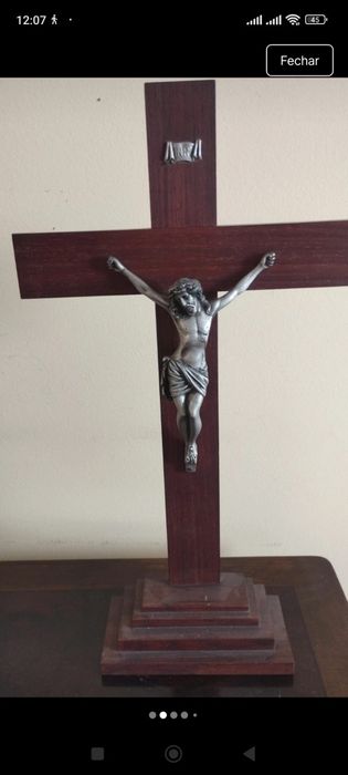 Crucifixo de mesa composto por uma cruz de madeira escura com uma base escalonada de vários níveis.A figura tridimensional do corpo de Cristo (corpus)