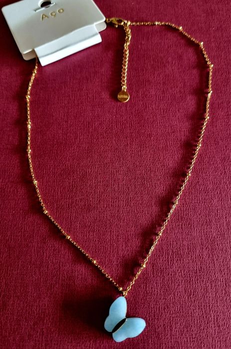 Colar dourado, em aço, malha com bolinhas e pingente borboleta azul.