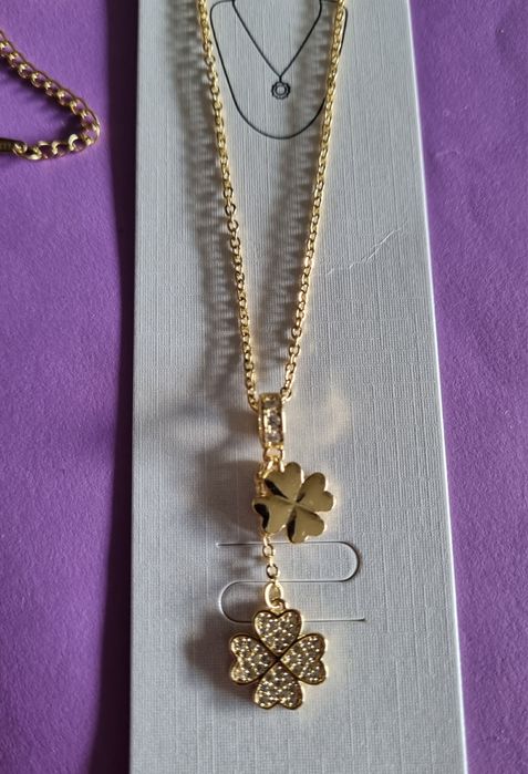 Colar dourado, em aço, com 2 trevos pendentes. Formato gravata.