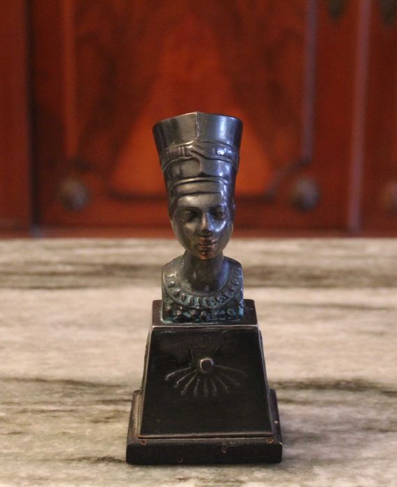 Busto de Nefertiti com 15,5cm de altura em metal sobre madeira.