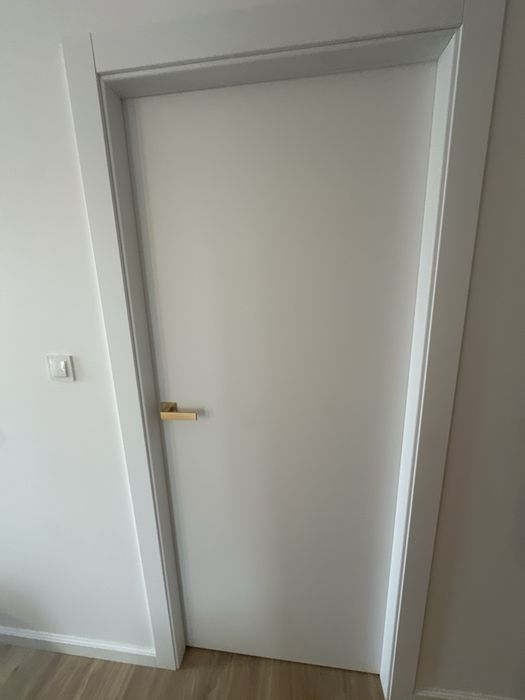 Białe drzwi bezprzylgowe z futryną i złotą klamką