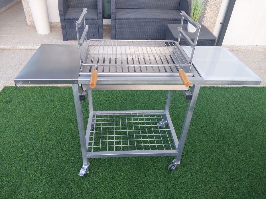 Churrasqueira com rodas, tem queimador  e grelha em inox  duas mesas de apoio uma em inox outra em nylon  e plataforma para lenha..