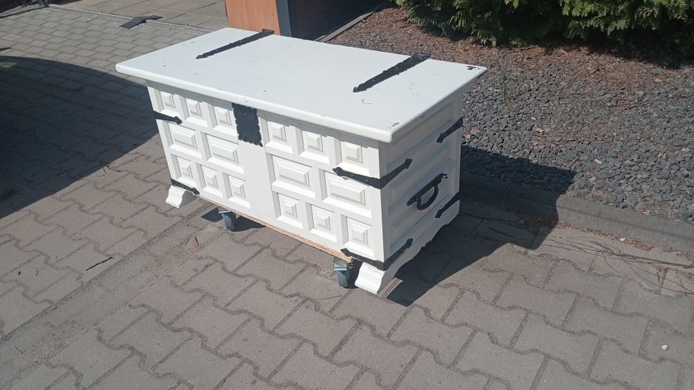 Biała duża skrzynia, kufer z czarnymi okuciami.