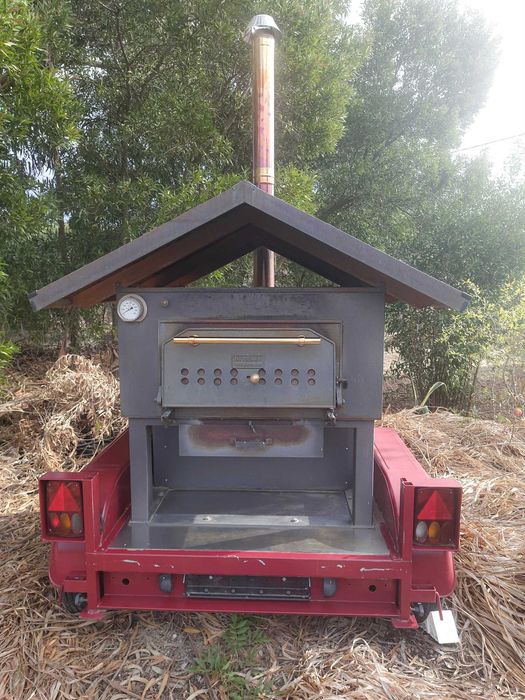 Forno de pedra a lenha profissional e móvel, montado sobre um chassis de reboque, concebido para eventos e utilização comercial em pequena escala.