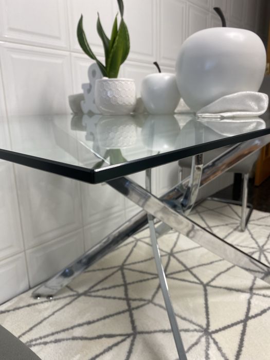 4 cadeiras mais mesa de jantar moderna  com um tampo em vidro transparente e uma elegante estrutura de pernas cruzadas em aço cromado brilhante.